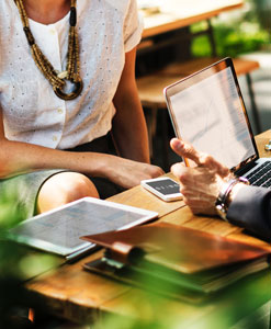 Two people sitting at a table with laptops and cell phones.