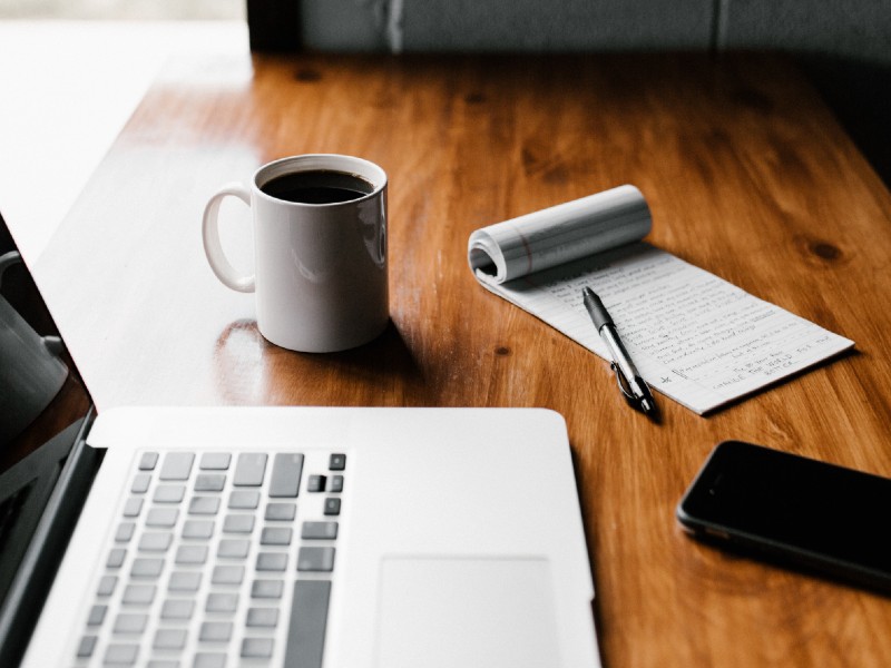 A cup of coffee and a cell phone on top of a desk.